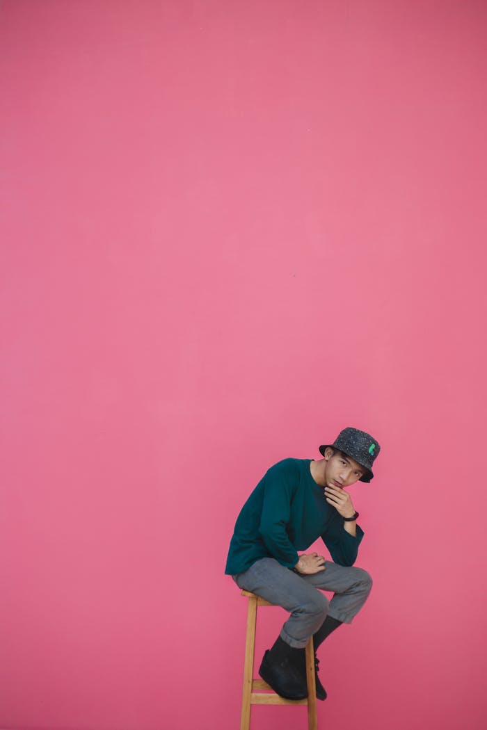 Man Sitting on Wooden Stool Against Pink Background